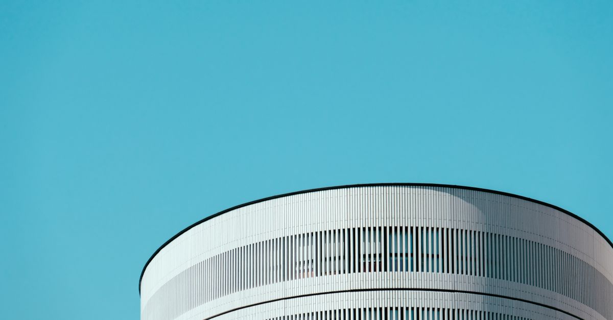 Minimalist architectural design with a focus on a cylindrical building under a clear blue sky.